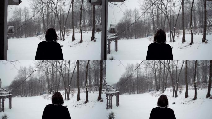 穿着黑色毛衣的年轻人站在屋外看雪景