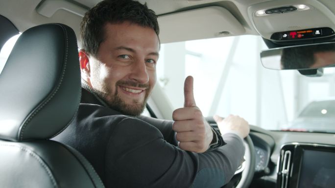 一张男子竖起大拇指坐在新车里微笑着
