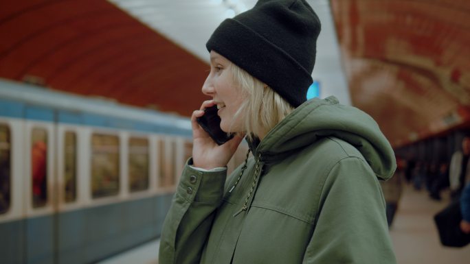 一位女孩在地铁站讲着电话，火车在后台经过。