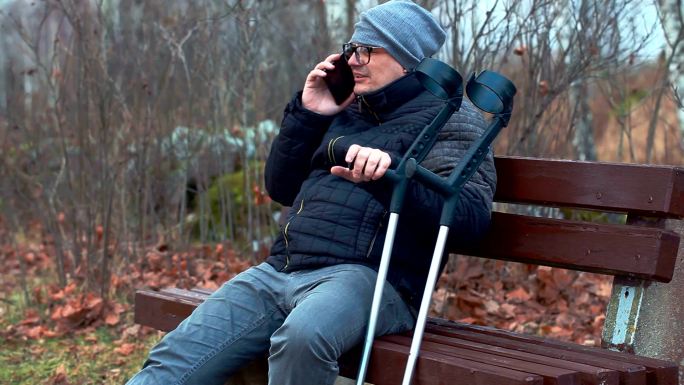 残疾人拄着拐杖，坐在长凳上使用智能手机