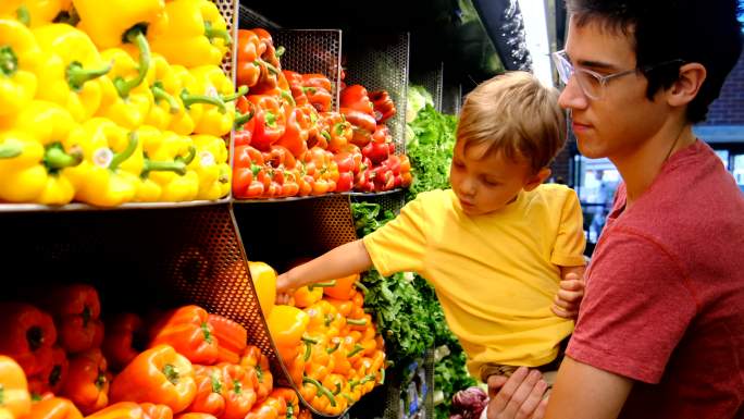 一对年轻的父子在超市的蔬菜区买蔬菜