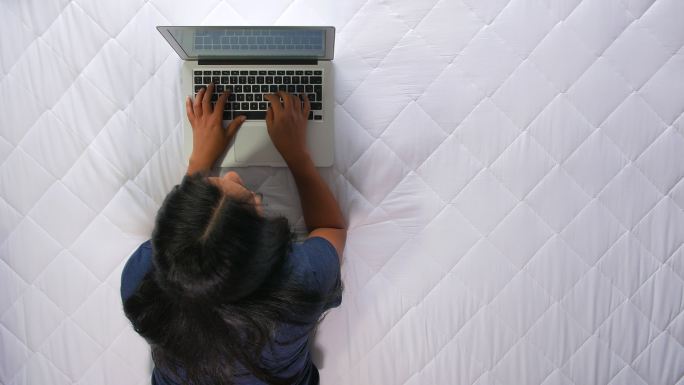 妇女坐在床上用笔记本电脑写文章