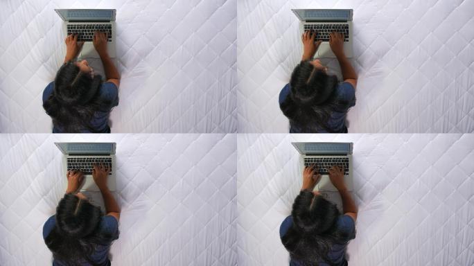妇女坐在床上用笔记本电脑写文章