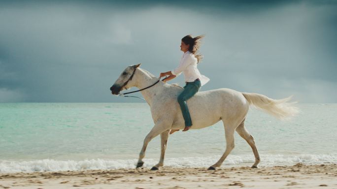 女子骑马沿着沙滩海岸线疾驰