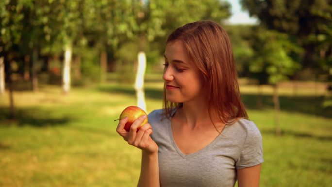 年轻女子在花园里吃着红苹果