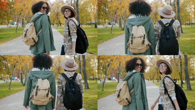 快乐的女孩朋友们背着背包在公园里散步，微笑着转向镜头