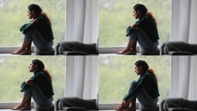 孤独的女人坐在窗台上看着外面的雨天