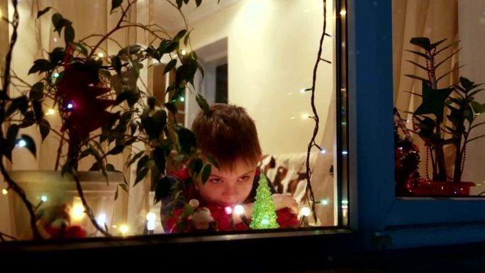 男孩等待圣诞节透过窗户看雪