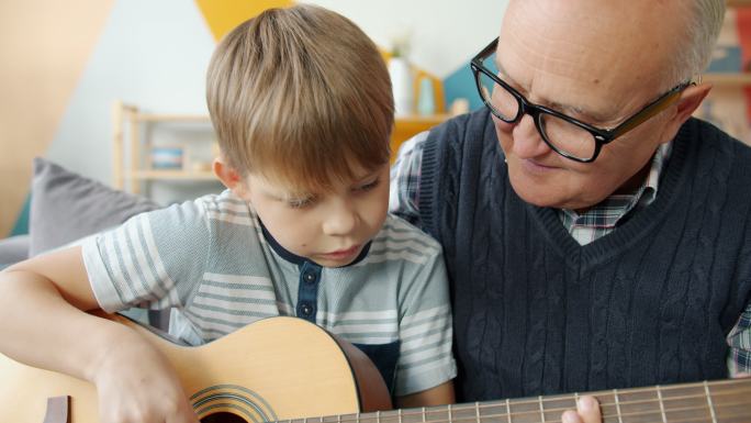 慈祥的爷爷在家帮助可爱的孩子学吉他