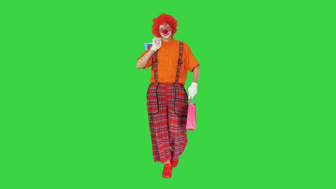 搞笑的小丑拿着购物袋在绿色屏幕上行走