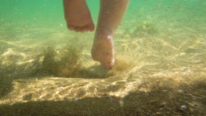 小婴儿的腿在水下踩沙子