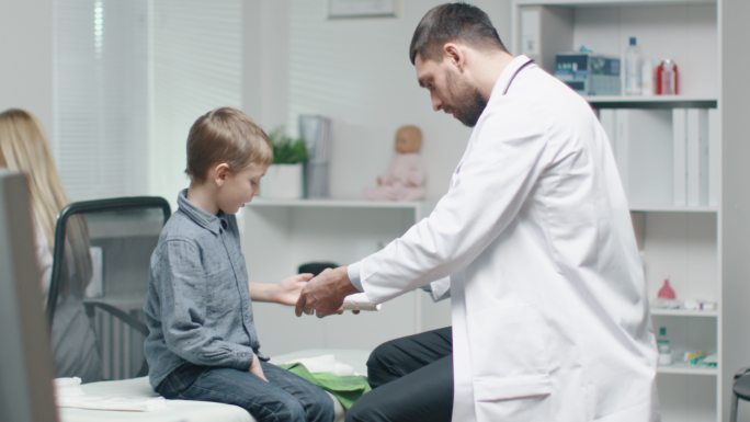 男医生从男孩治愈的手上取下石膏。