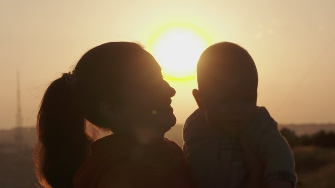 日落时快乐的母亲和儿子的剪影