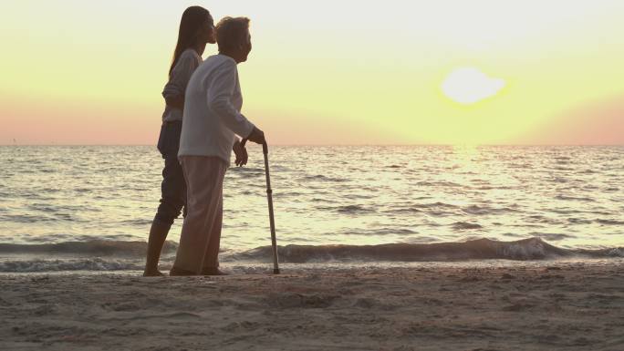 在日落海滩背景下帮助母亲散步
