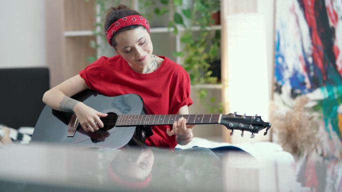年轻女子坐在家里的客厅里，弹原声吉他