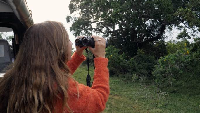 女子在狩猎旅行中用双筒望远镜寻找野生动物