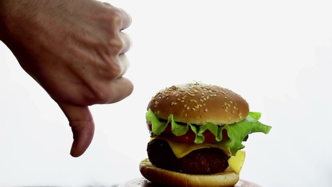 在新鲜多汁汉堡的背景上向下伸出拇指