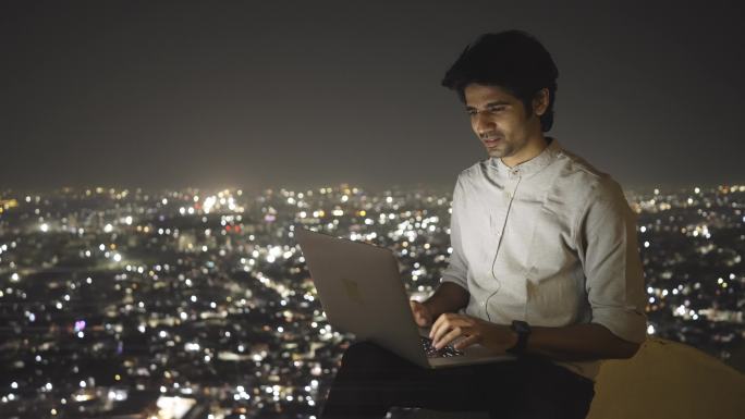 一名男性坐在屋顶上用笔记本电脑