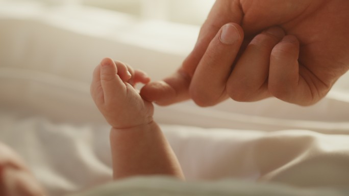 新生儿躺在婴儿床上握住母亲的手指