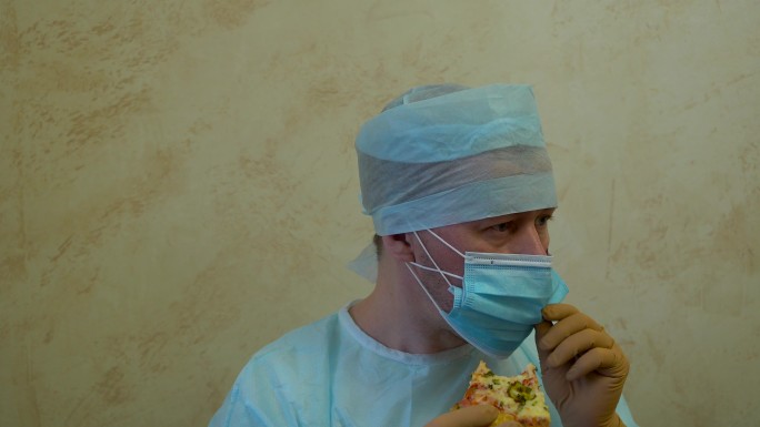 男医生穿着医疗服，戴着口罩和手套偷吃披萨