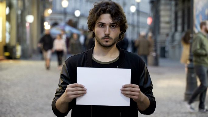 年轻人在街上举着一张空白的纸