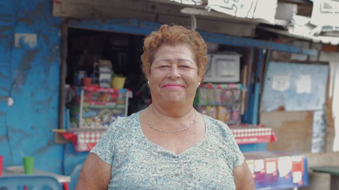 一位年长的女性微笑着站在一个食品摊前