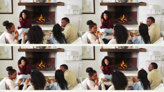 一家人坐在客厅的沙发上，挨着篝火吃披萨