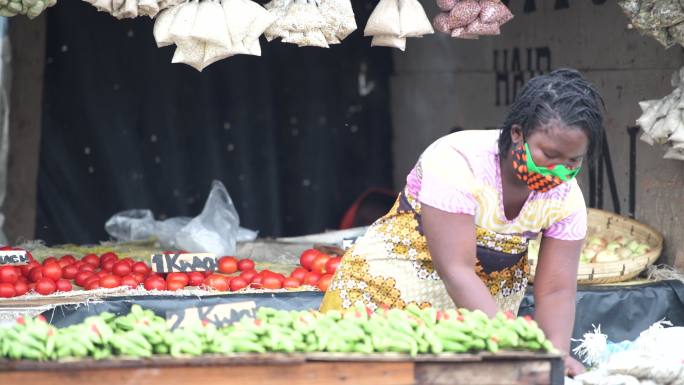 戴口罩的年轻女子在市场摊位上包装蔬菜