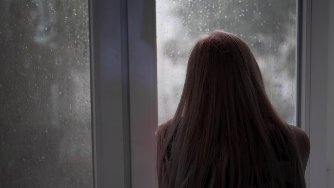 一个孤独的女孩坐在家里看着窗外落下的雨滴
