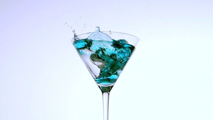 冰块掉进蓝色液体的鸡尾酒杯里