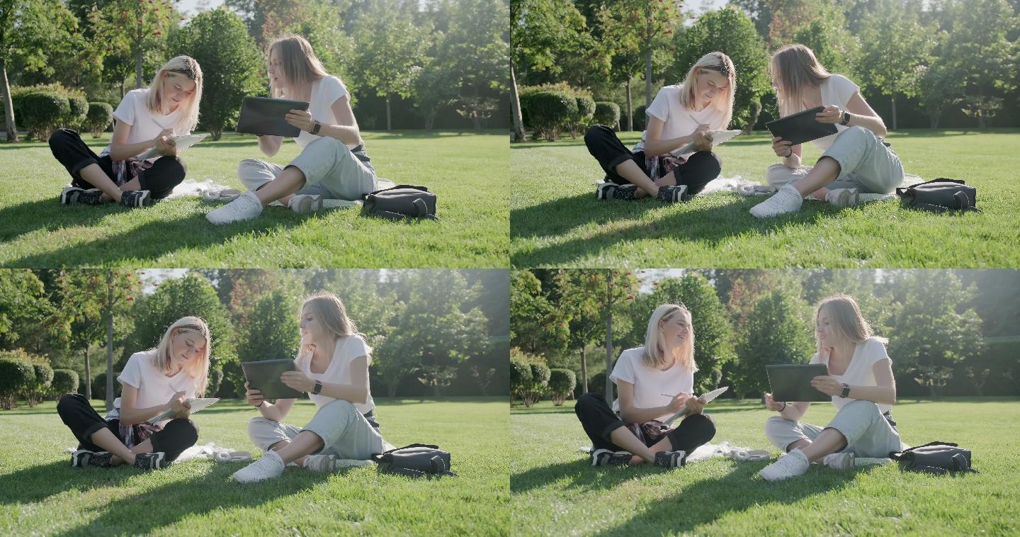 女孩坐在公园的绿色草坪上看平板电脑