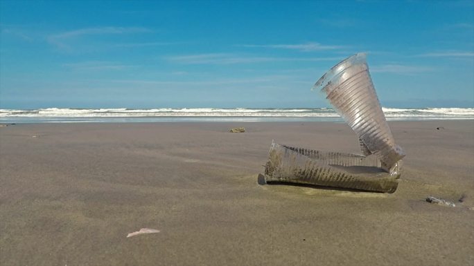 扔在海滩上随风摆动的塑料杯