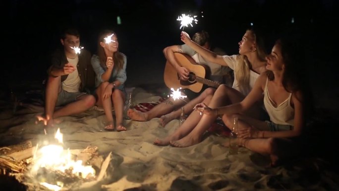 海滩上的朋友们在日落时分拿着火花庆祝
