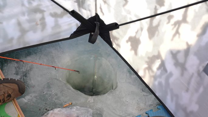 冬天结冰河面户外冰钓帐篷里砸冰窟窿钓鱼
