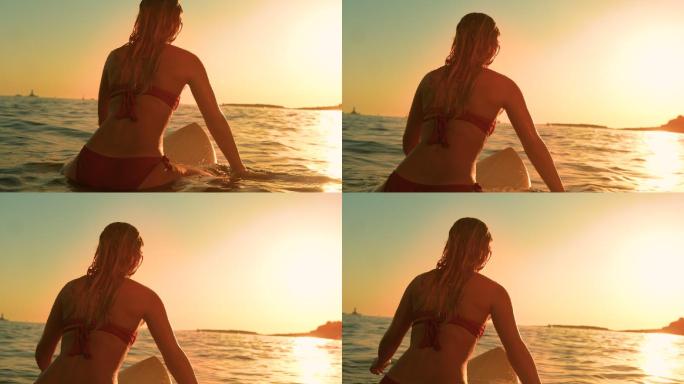 身穿红色比基尼的女子坐在冲浪板上看日落