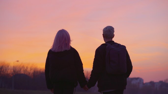 十几岁的情侣手牵手在河边欣赏着日落