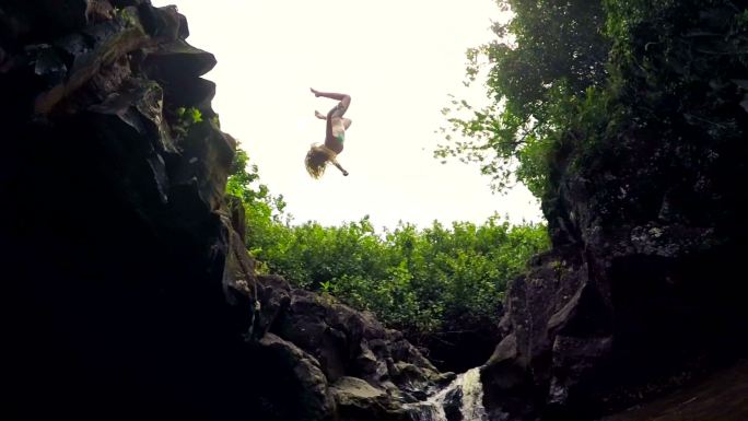 年轻女子后空翻从悬崖上跳入水中。