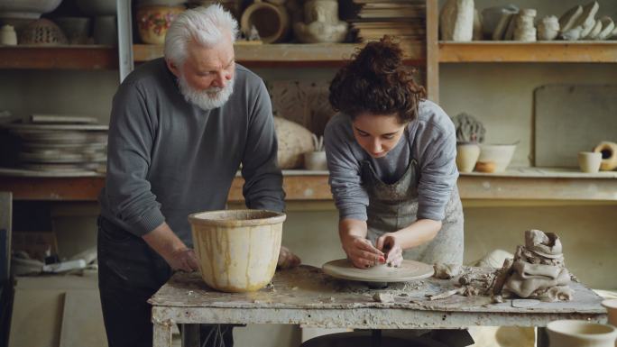 爷爷正在教年轻女孩做陶器手工。