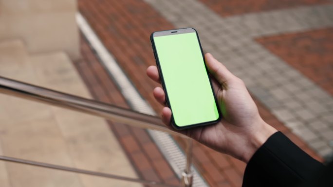 一个人手持智能手机在绿色屏幕上滑动