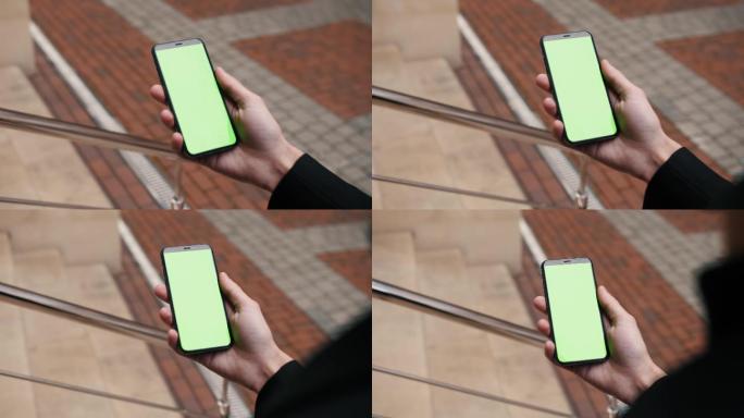一个人手持智能手机在绿色屏幕上滑动