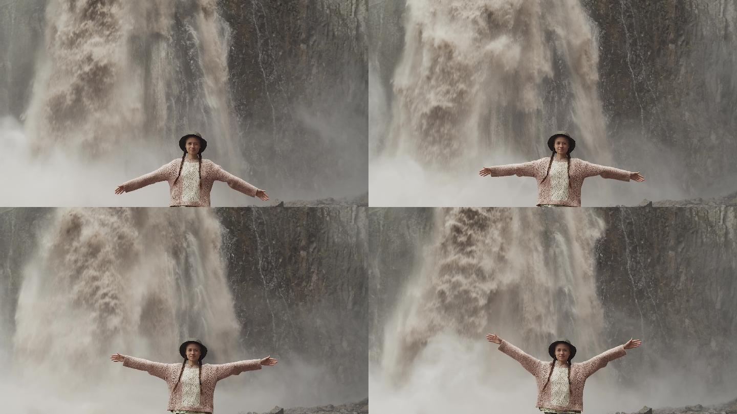 穿着毛衣、扎着辫子的年轻女游客站在瀑布前