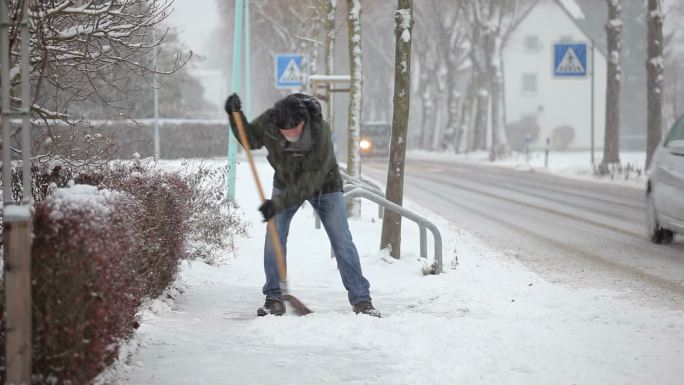 铲人行道上的积雪老人降雪雪中铲雪冬天来临