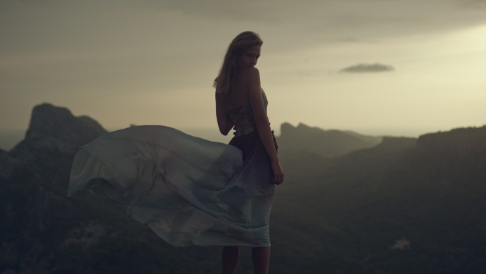 穿着夏日长裙的年轻女子站在悬崖上