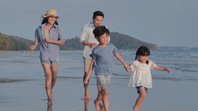 父母和孩子沿着海边的沙滩快乐地奔跑