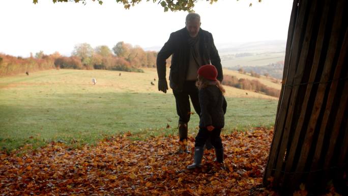 爷爷和孙女在秋日散步时踢树叶