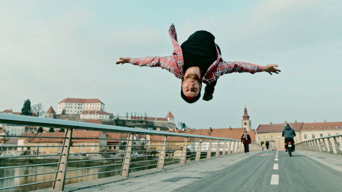 一个男孩在城市的桥上做后空翻的超慢镜头。