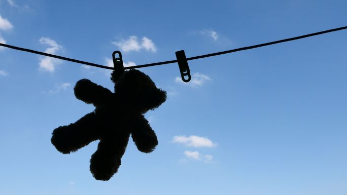 泰迪熊挂在晾衣绳上的剪影，天空湛蓝。