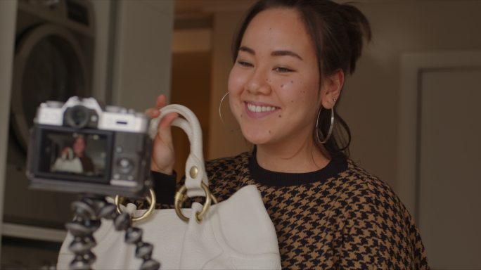 一名年轻女子在家录制美容博客时展示时尚包