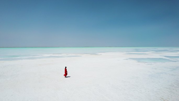 身穿红色连衣裙的女子在盐湖上行走
