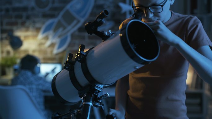 小男孩在晚上通过望远镜看东西